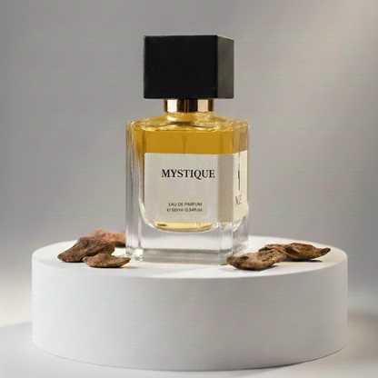 Mystique eau de parfum bottle with black cap on white round pedestal surrounded by dried brown flower petals