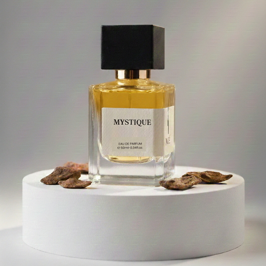 Mystique eau de parfum bottle with black cap on white round pedestal surrounded by dried brown flower petals