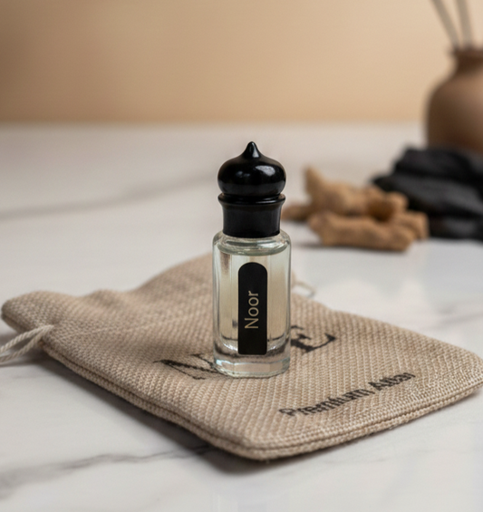 Small glass bottle labeled Noor with black cap on beige jute pouch on marble surface